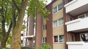 A multi-story residential building with brick and white exterior walls, balconies, and a garden area with trees and shrubs. - Luchtbergstraße 1 (Bremen)