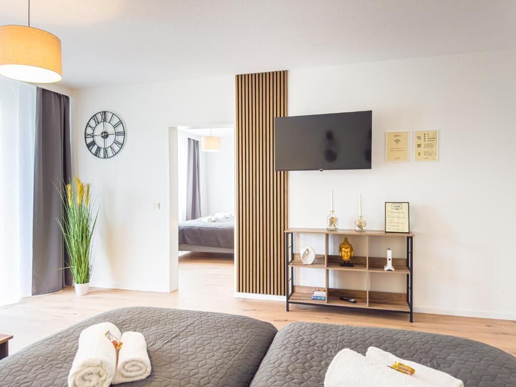 A modern hotel room with a bed, a TV, a clock, and a plant.