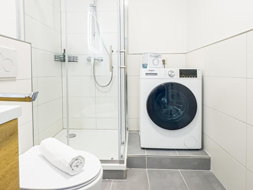 A bathroom with a shower, toilet, and a front-loading washing machine.