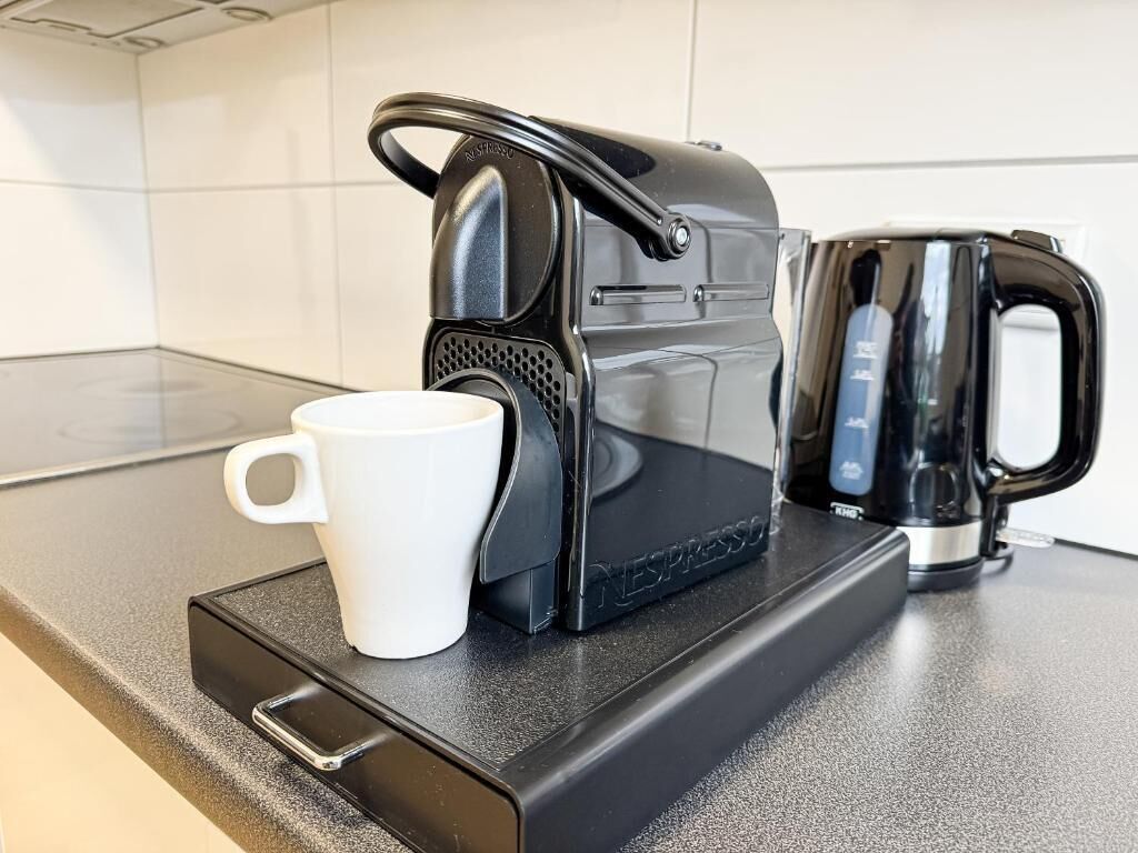 A black Nespresso coffee machine on a countertop with a white mug and a black electric kettle.