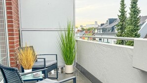A balcony with a table and chairs, a potted plant, and a view of buildings. - Luchtbergstraße 1 (Bremen)