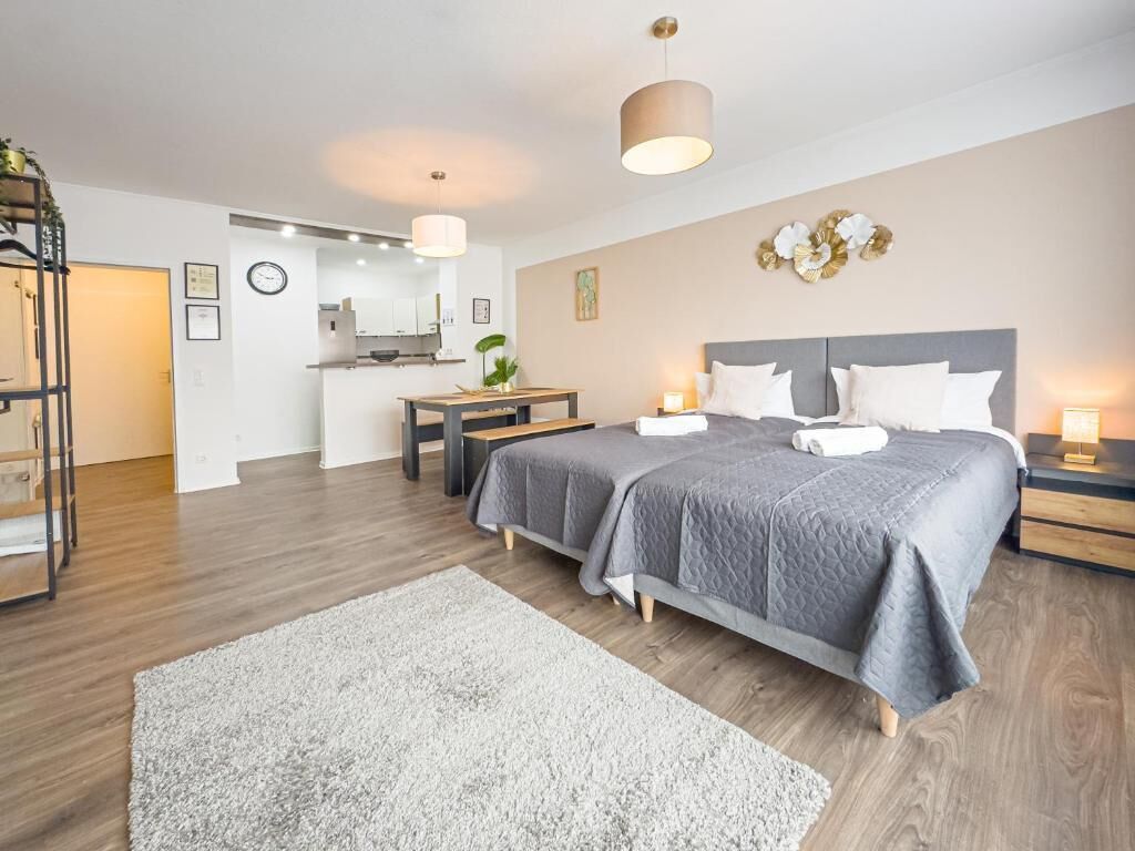 A modern hotel room with a large bed, a desk, and a kitchenette.
