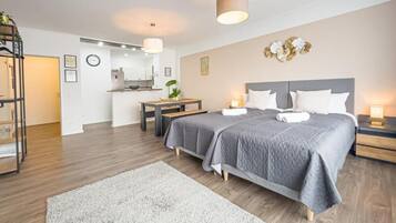 A modern hotel room with a large bed, a desk, and a kitchenette.