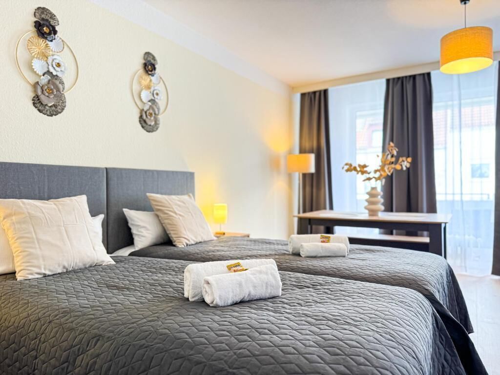 Een hotelkamer met twee bedden, een bureau, een lamp en een raam met gordijnen.