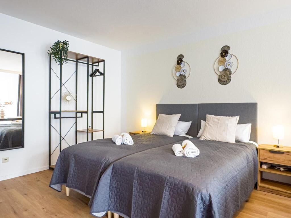 A hotel room with two beds, a wooden floor, a wall-mounted TV, a plant, and decorative wall art.