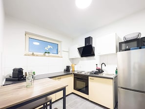 A modern kitchen with a wooden table, stainless steel appliances, and a window with a view of the sky. - Luchtbergstraße 1 (Bremen)