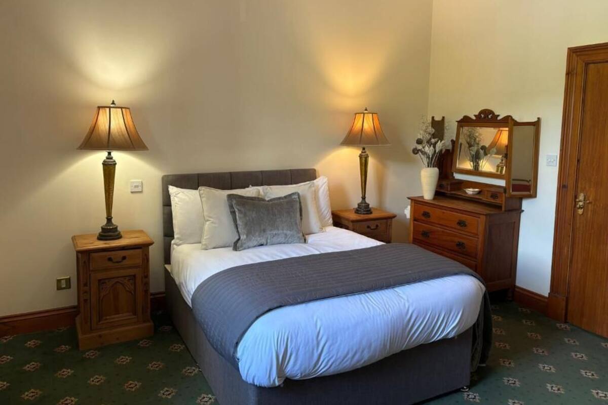 A bedroom with a bed, two bedside lamps, a dresser, a mirror, and a door.