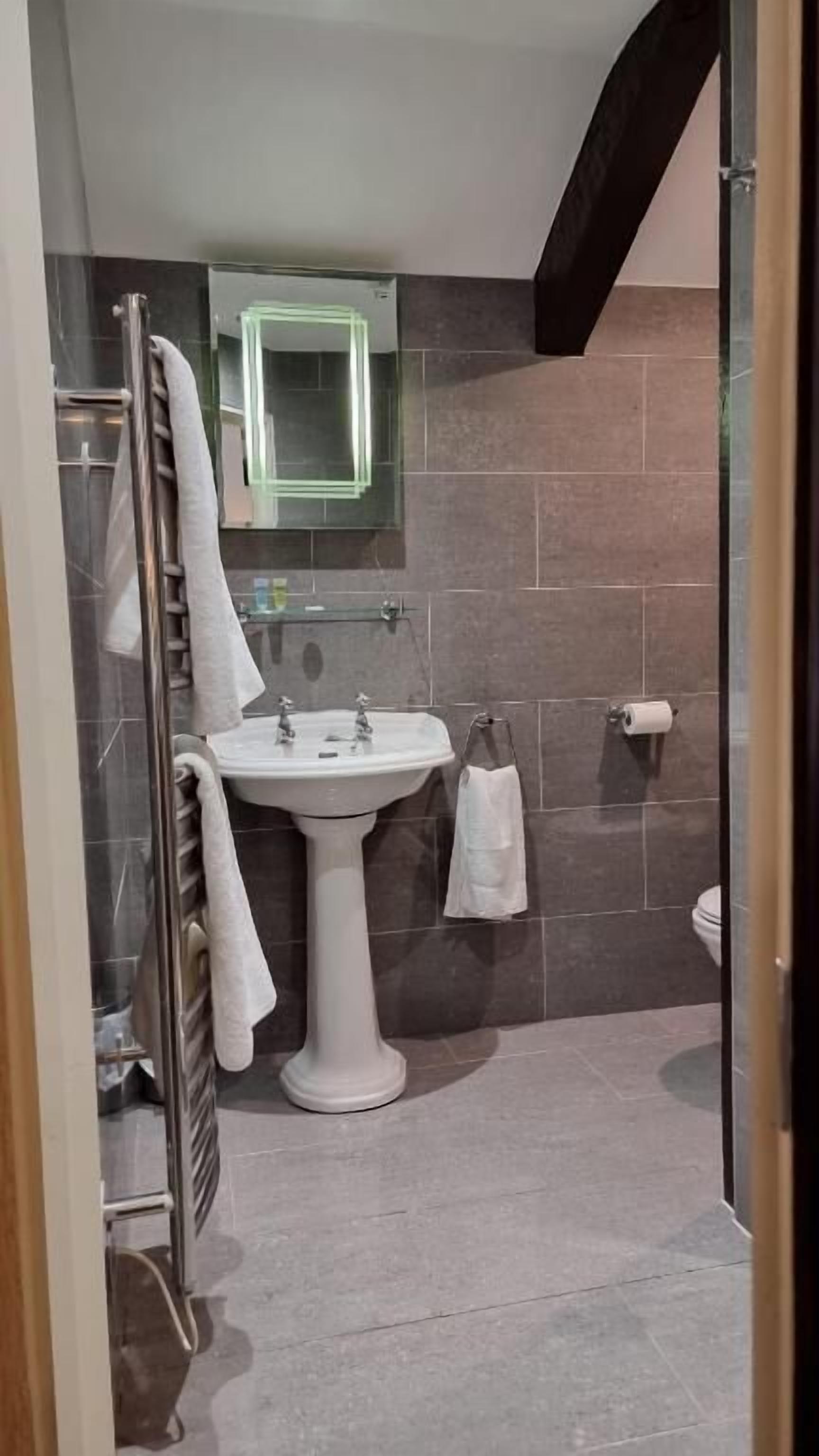 A modern bathroom with a pedestal sink, a glass shower enclosure, and a toilet.