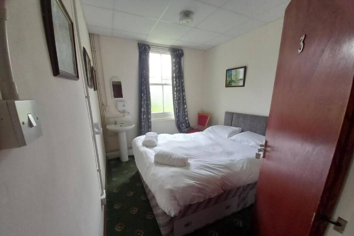 A hotel room with a bed, a window with curtains, a sink, and a door.