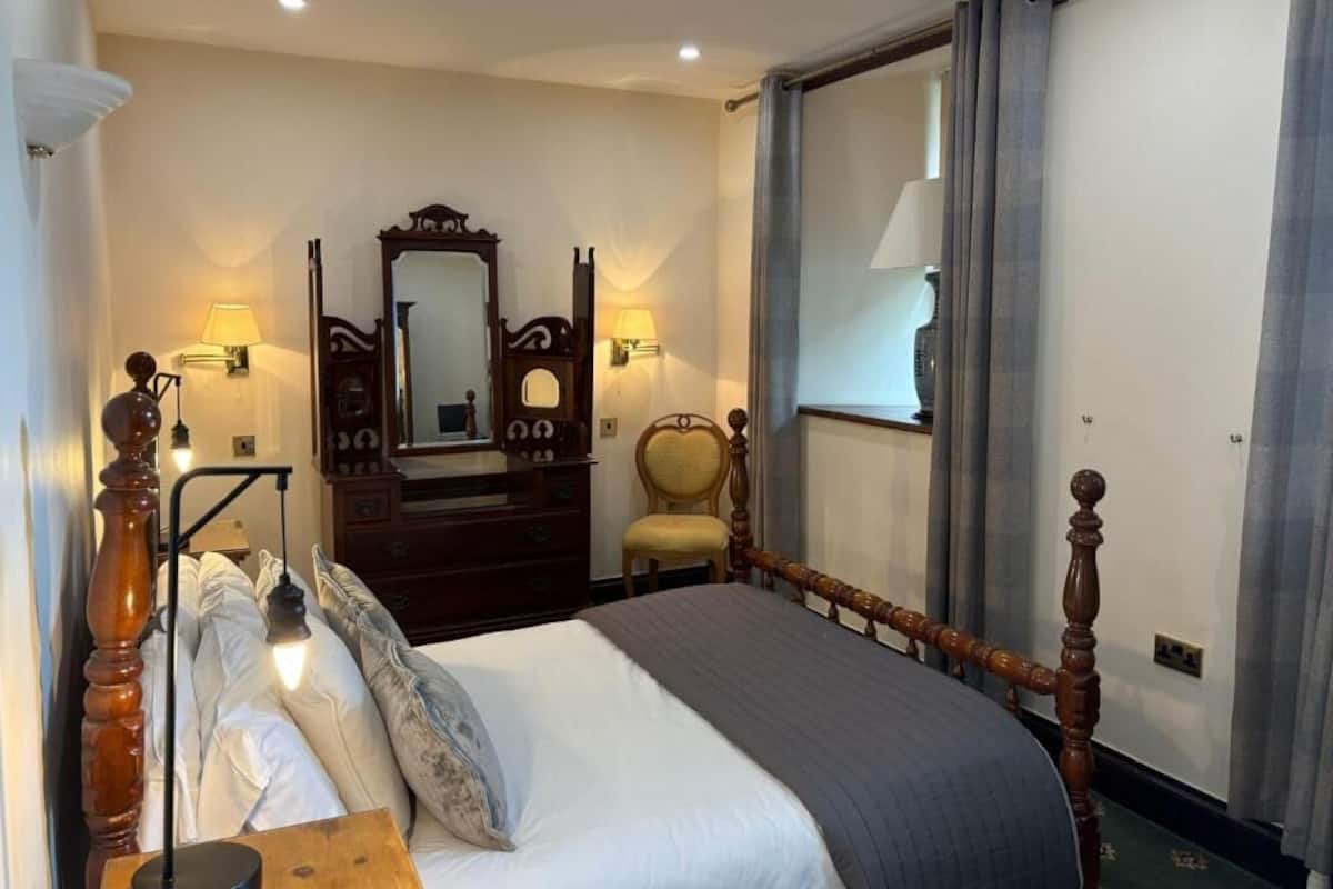 A hotel room with a bed, a dresser, a chair, a mirror, and a window with curtains.