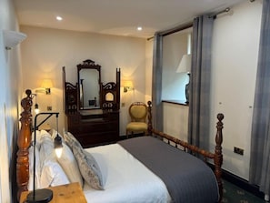 A hotel room with a bed, a dresser, a chair, a mirror, and a window with curtains. - Craig Y Nos Castle (Swansea)