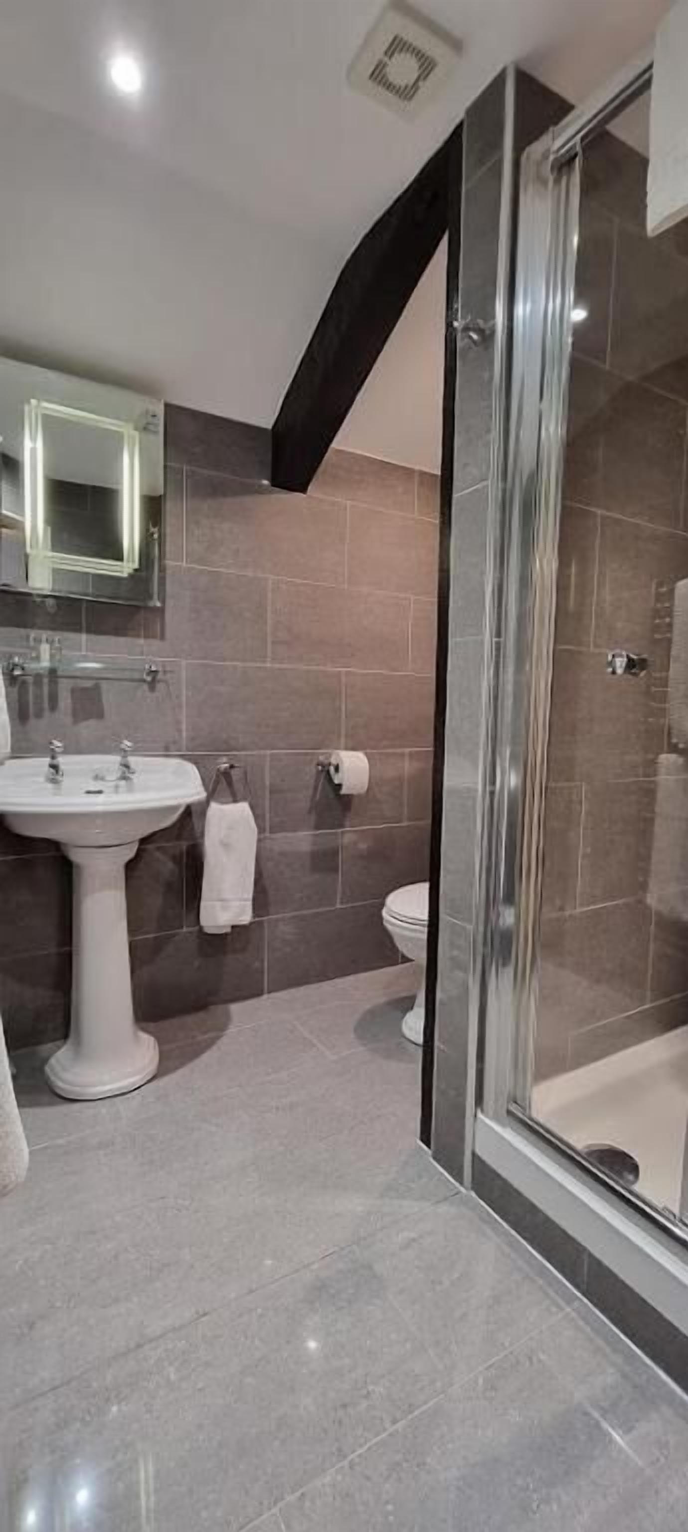 Un baño moderno con ducha envuelta en vidrio, lavamanos pedestal y retrete.