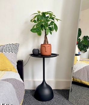 A potted plant on a small black table with a face design, a speaker, and a bed with patterned bedding. - Room-lovely Room In Brixton (London)