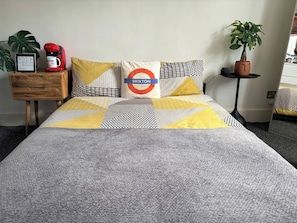 A bed with a grey and yellow patterned bedspread, a pillow with a London Underground logo, a red coffee maker, and a potted plant. - Room-lovely Room In Brixton (London)