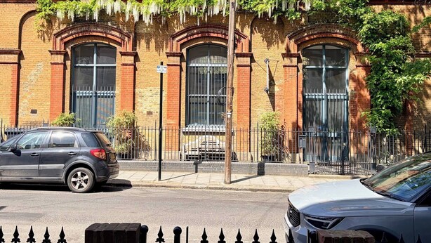 Un bâtiment en briques doté de grandes fenêtres et d’une entrée fermée par un portail.