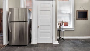 Una cocina con un refrigerador de acero inoxidable, una puerta blanca y un ventanal con persianas.
