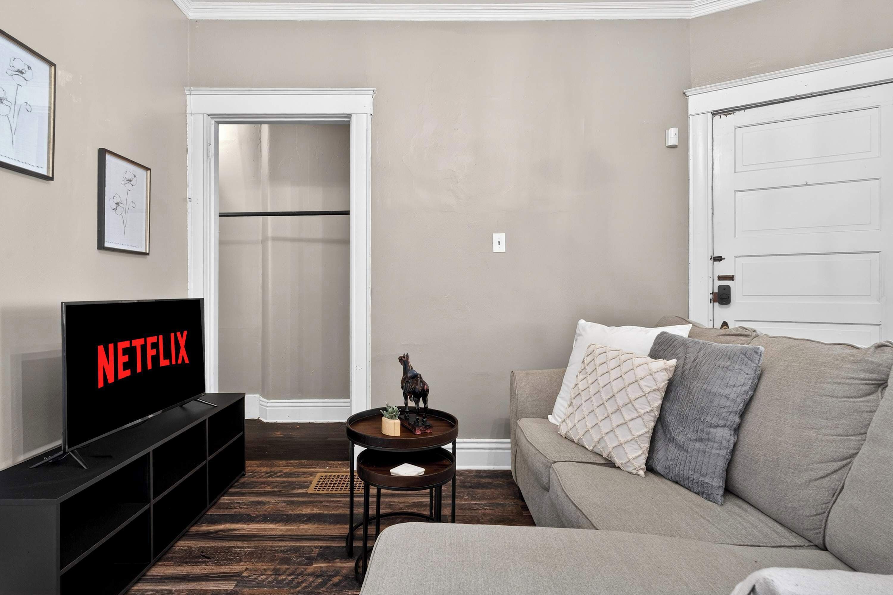 Un salon avec un téléviseur affichant le logo « NETFLIX », un canapé, une table basse et une porte.