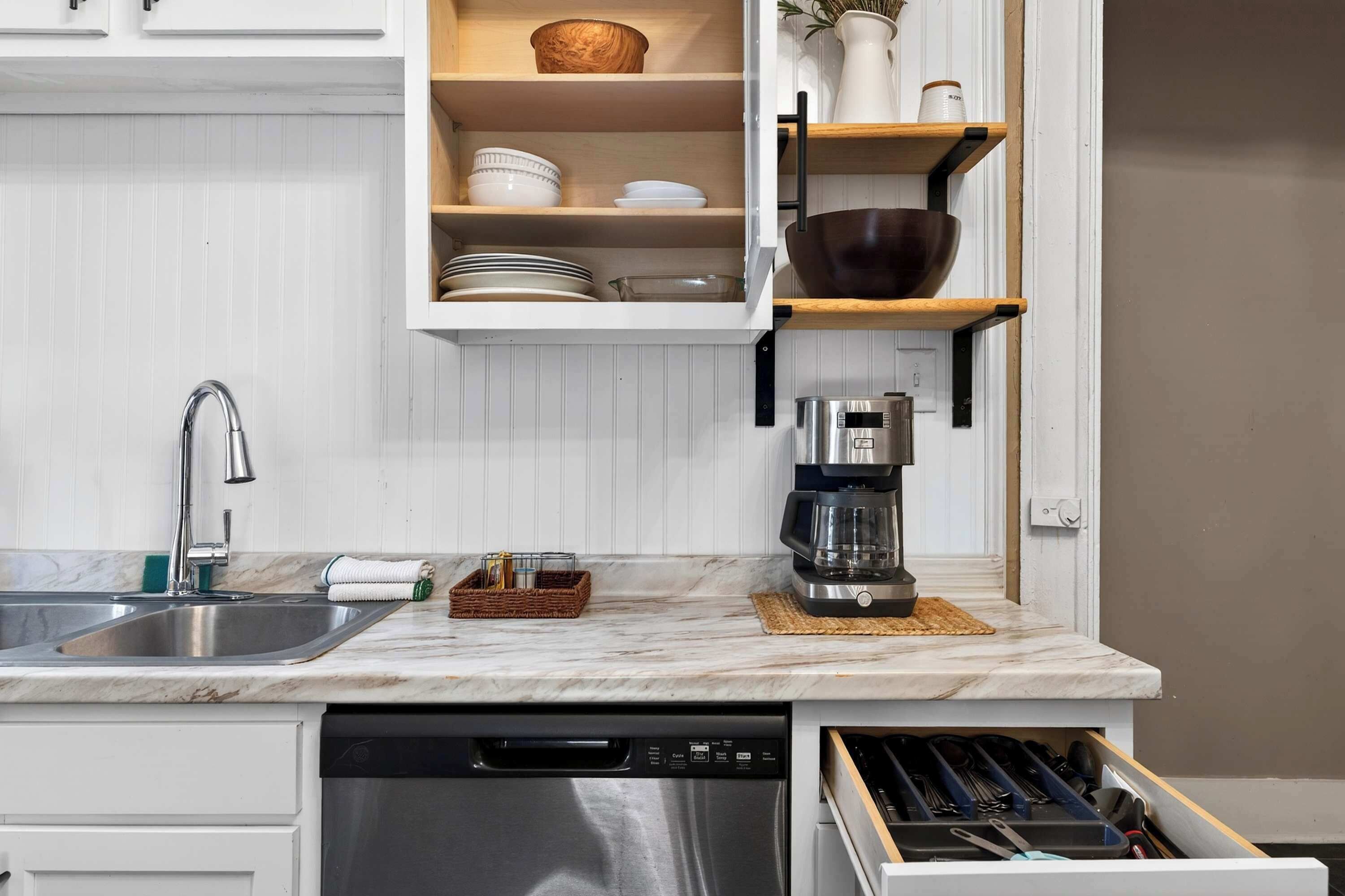A kitchen with a dishwasher, a coffee maker, and a built-in shelf with dishes and bowls.