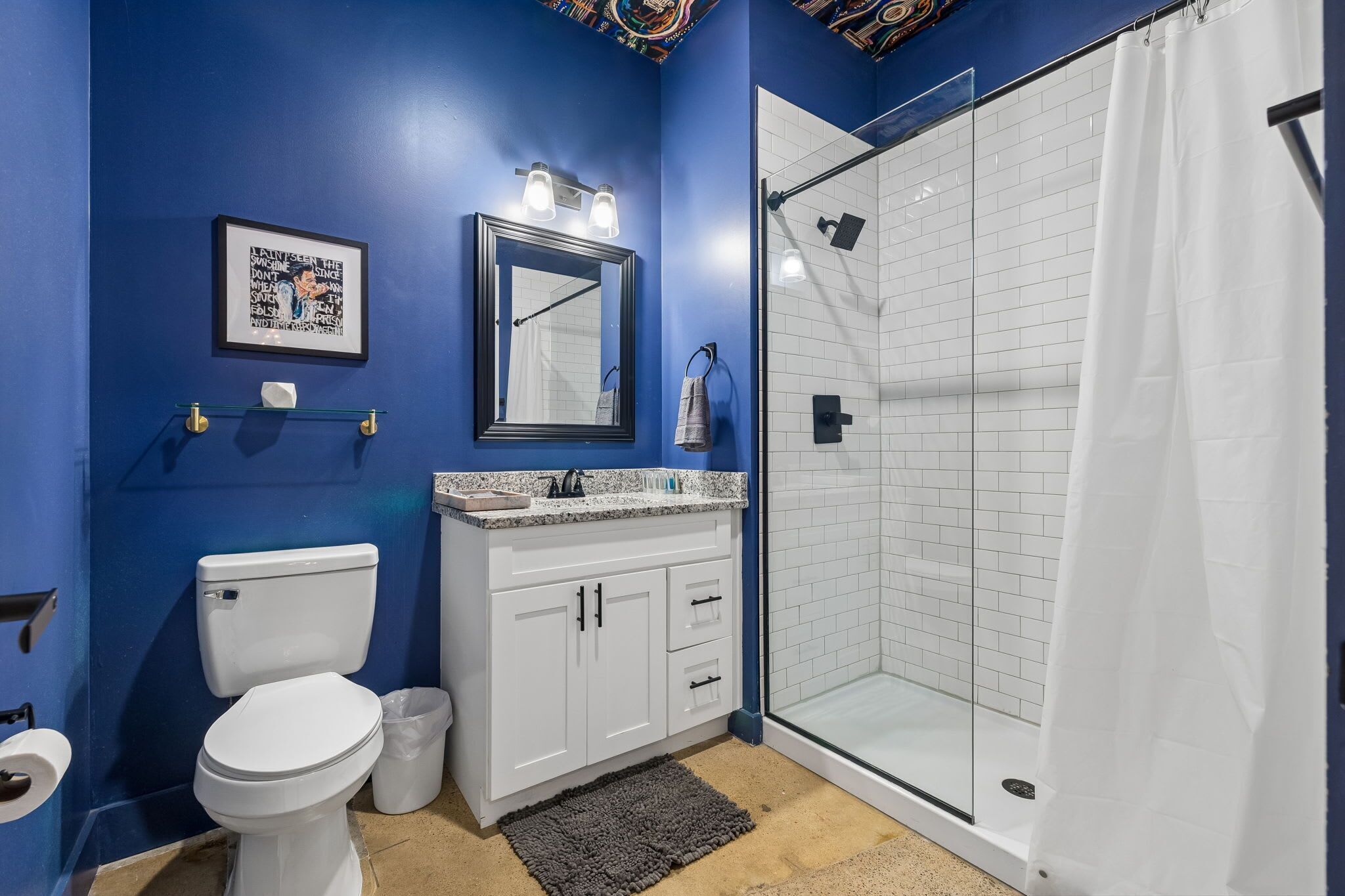 A bathroom with a blue wall, white toilet, and a glass shower enclosure.