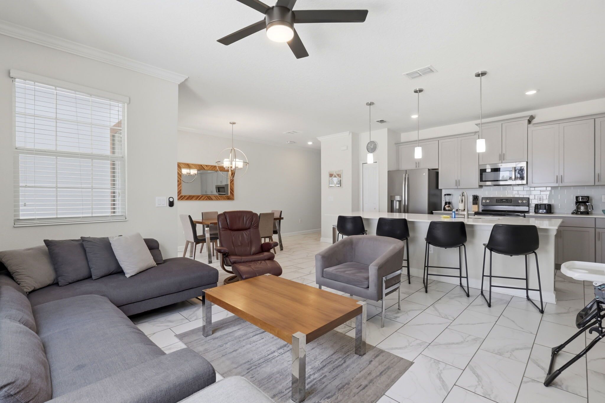 A modern living room with a sofa, armchairs, a coffee table, and a dining area with chairs and a chandelier.