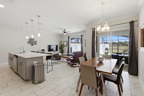 A modern kitchen with a central island, dining area with a table and chairs, a TV, and a ceiling fan. - New! Oasis Retreat Escape - Private Pool - Walk to Clubhouse - Sleeps 10 (Four Corners)