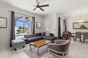 A modern living room with a sectional sofa, ottoman, coffee table, and a dining area with chairs and a table. - New! Oasis Retreat Escape - Private Pool - Walk to Clubhouse - Sleeps 10 (Four Corners)