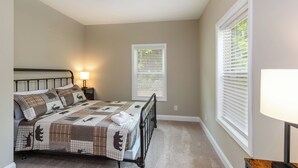 A bedroom with a bed, a nightstand, a lamp, and a window with blinds.