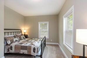 A bedroom with a bed, a nightstand, a lamp, and a window with blinds.