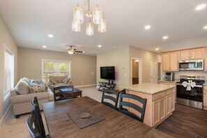 A modern kitchen with built-in appliances, a dining area with a wooden table and chairs, and a living room with a sofa and TV.