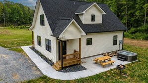 A two-story house with a porch, a hot tub, and a picnic table.