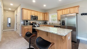 A modern kitchen with wooden cabinets, stainless steel appliances, a granite countertop, and two bar stools.
