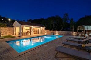 Ein Schwimmbecken mit Liegestühlen, einer überdachten Terrasse und einer Steinmauer.