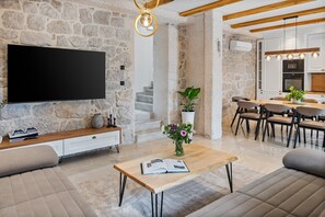 Ein modernes Wohnzimmer mit Steinwand, Flachbildfernseher, Holztisch und Essbereich mit Küche im Hintergrund.