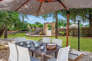An outdoor patio with a table set for dining, surrounded by chairs, under a large umbrella. - Casolare Di Puglia With Private Pool (Noci)