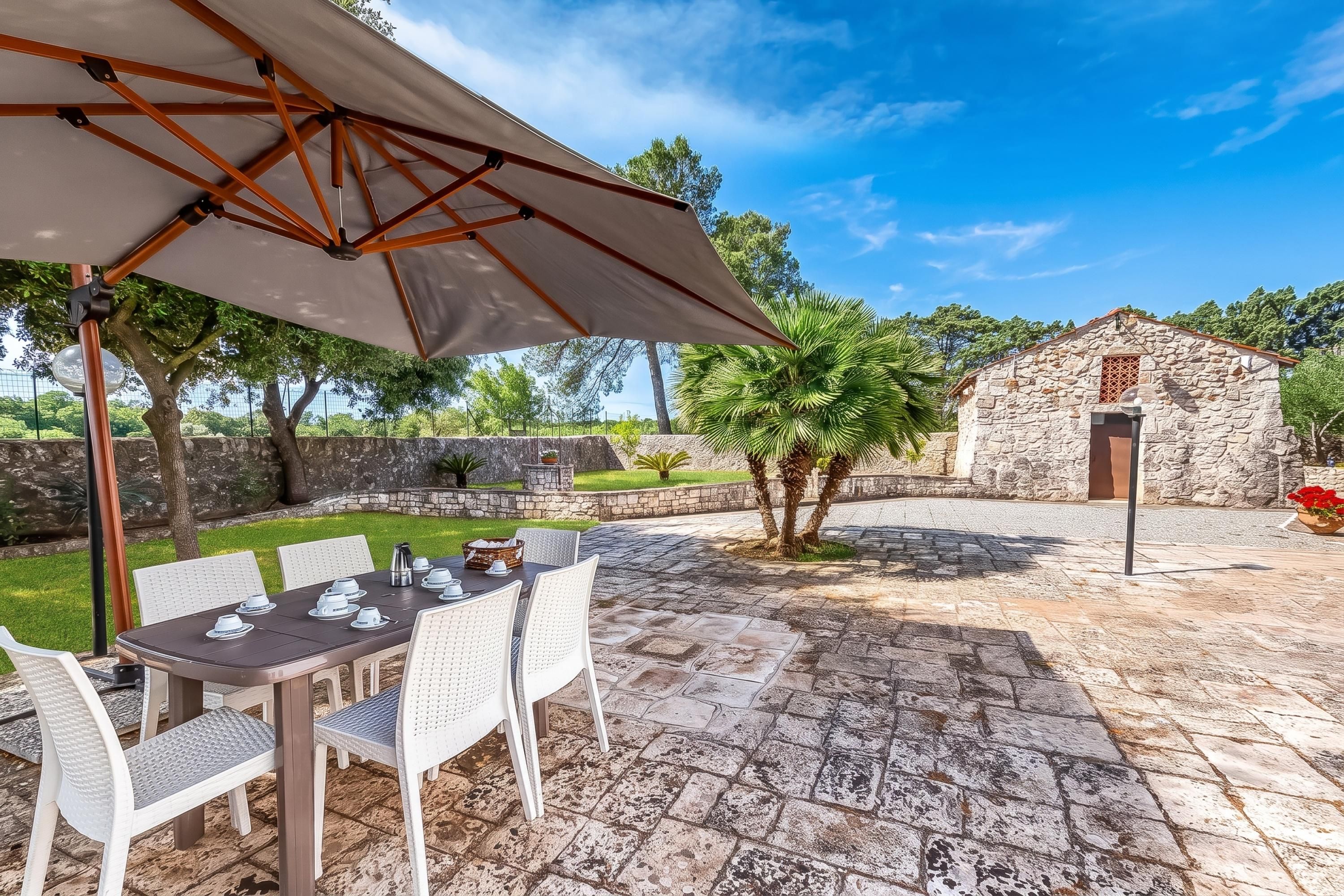 Une terrasse extérieure avec une table dressée pour le repas, entourée de chaises, et un parasol offrant de l’ombre.