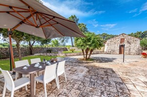 Un patio al aire libre con una mesa lista para comer, rodeada de sillas y una sombrilla que da sombra.