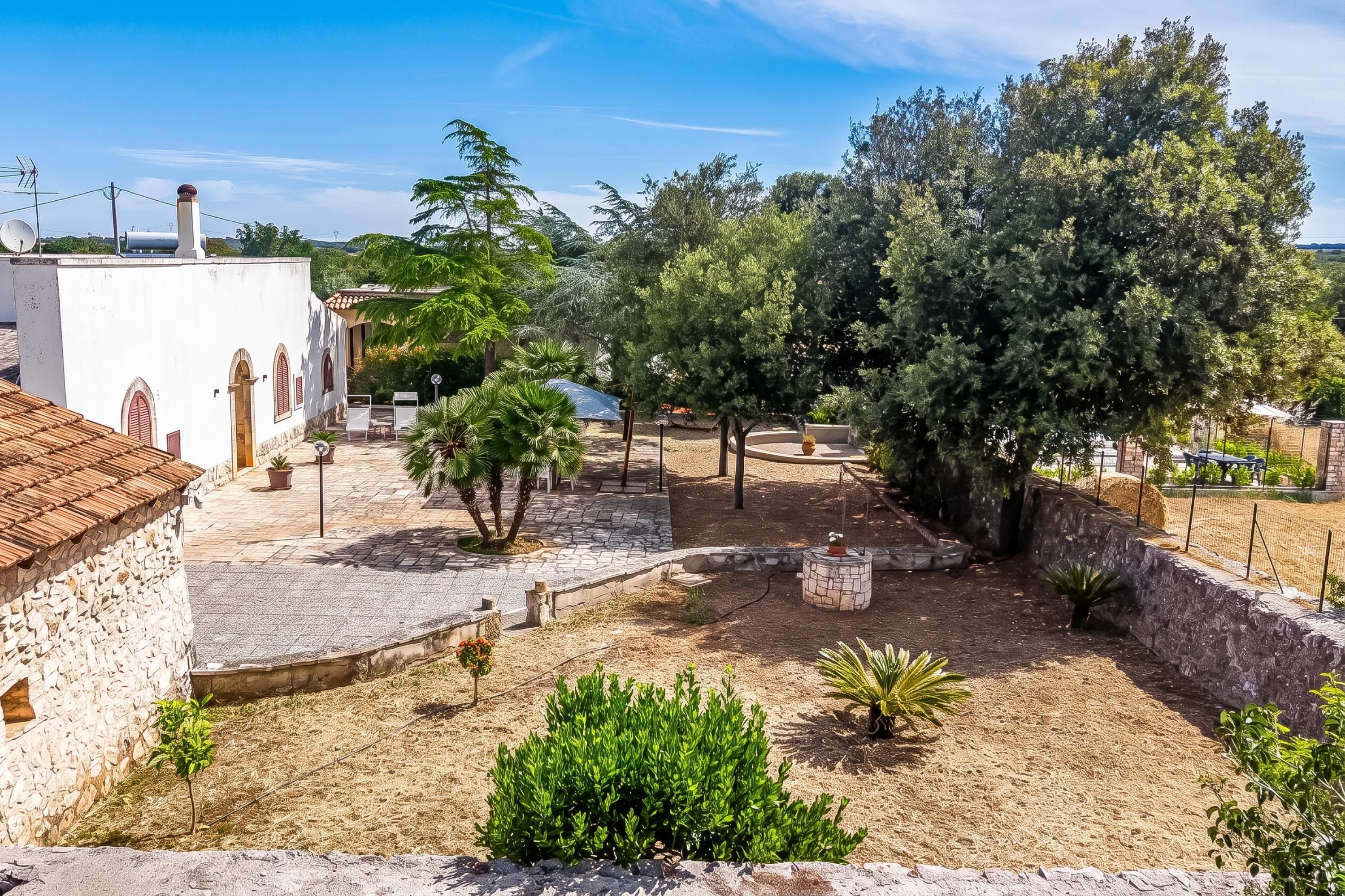 A courtyard with stone walls, potted plants, and a white building with a tiled roof.