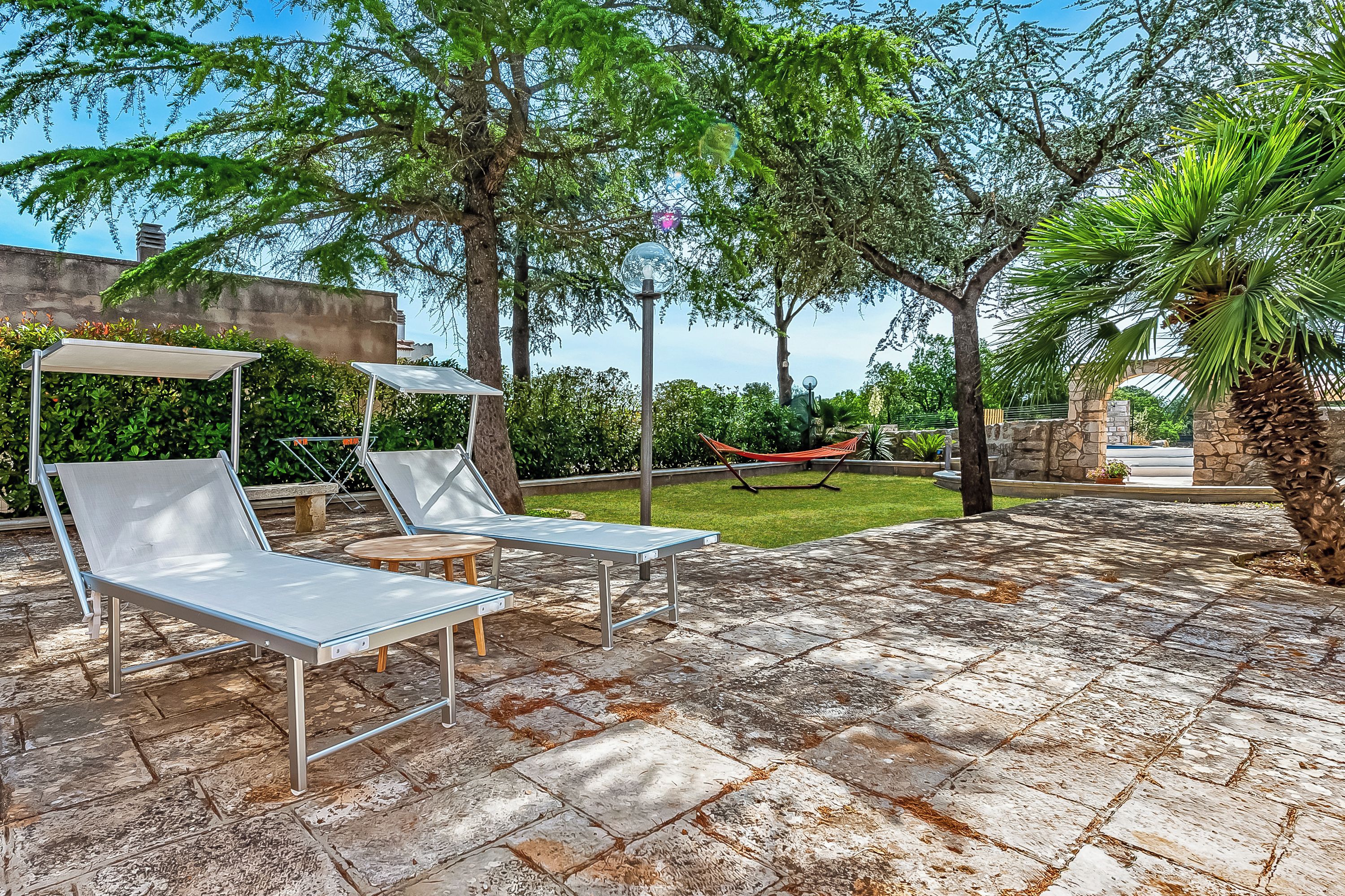 An outdoor patio with lounge chairs, a hammock, and a stone-tiled floor.