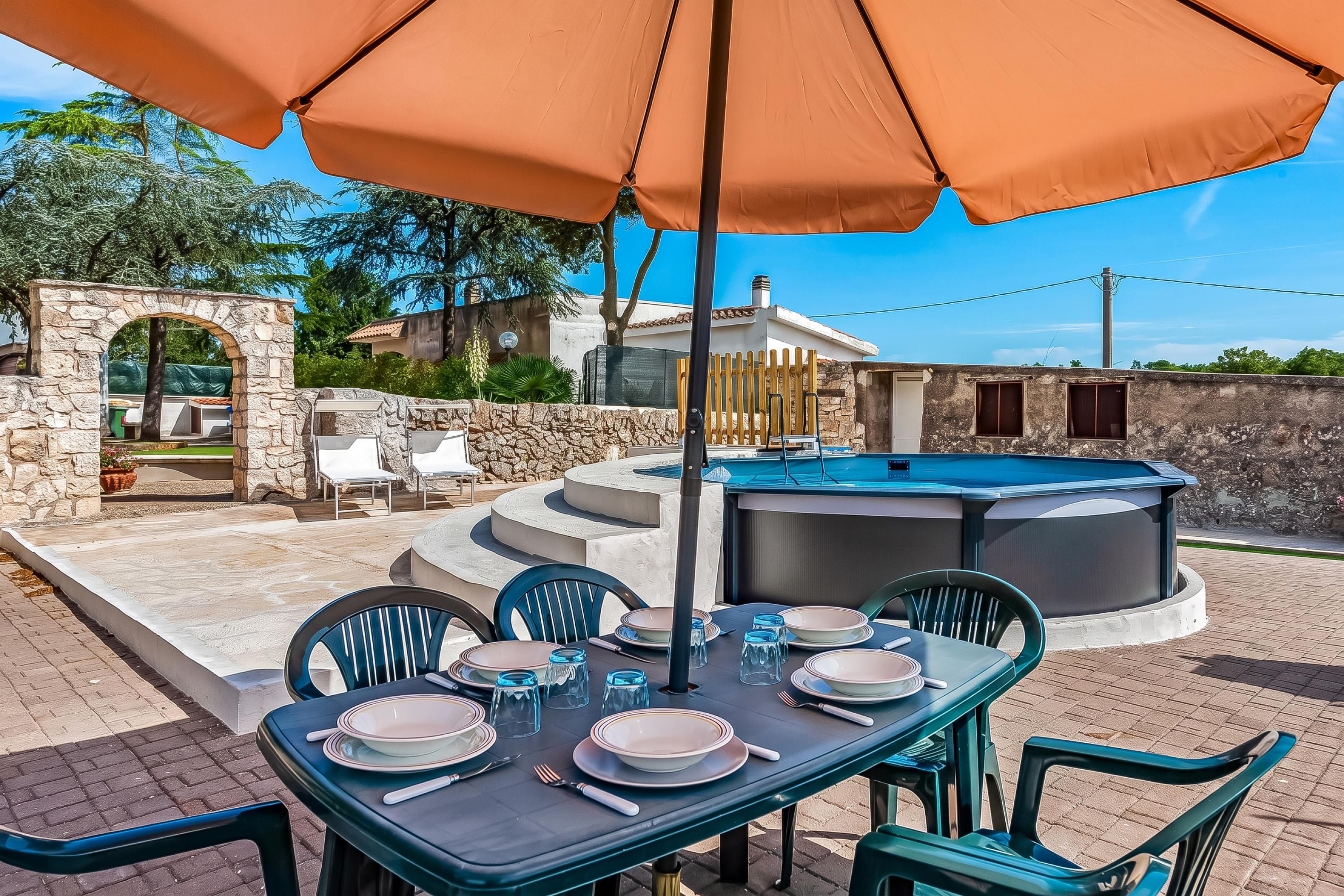 An outdoor dining area with a table set for four, surrounded by chairs, under a large umbrella.
