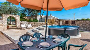 An outdoor dining area with a table set for four, surrounded by chairs, under a large umbrella.