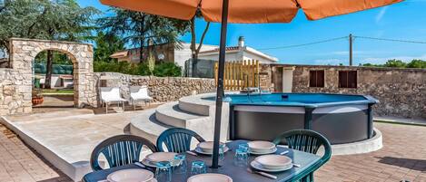 An outdoor dining area with a table set for four, surrounded by chairs, under a large umbrella.