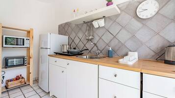 A modern kitchen with a microwave, toaster, and refrigerator, wooden cabinets, a sink, and a clock on the wall.