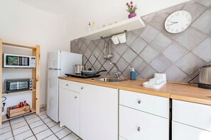 Una cocina moderna con microondas, tostadora y refrigerador, armarios de madera, un lavamanos y un reloj en la pared.