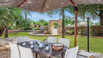 An outdoor patio with a table set for dining, surrounded by chairs, under a large umbrella.