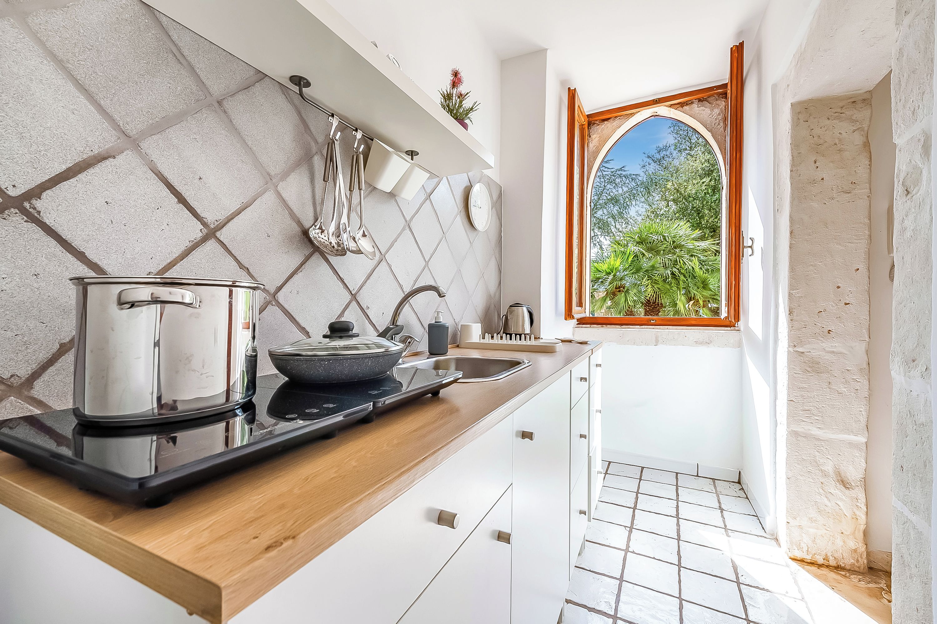 A kitchen with a stove, sink, and window with a view of greenery.