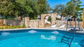 A swimming pool with stone walls, a stone archway, and lounge chairs.