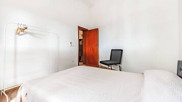A bedroom with a bed, a chair, a wardrobe, and a door leading to another room.