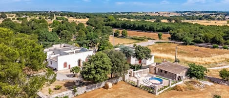 A residential property with a swimming pool, surrounded by trees and open fields.