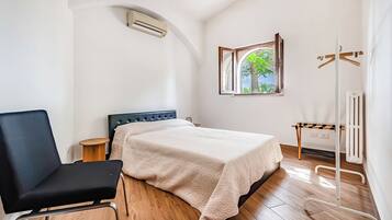 A bedroom with a bed, a chair, a radiator, and a window with a view of trees.