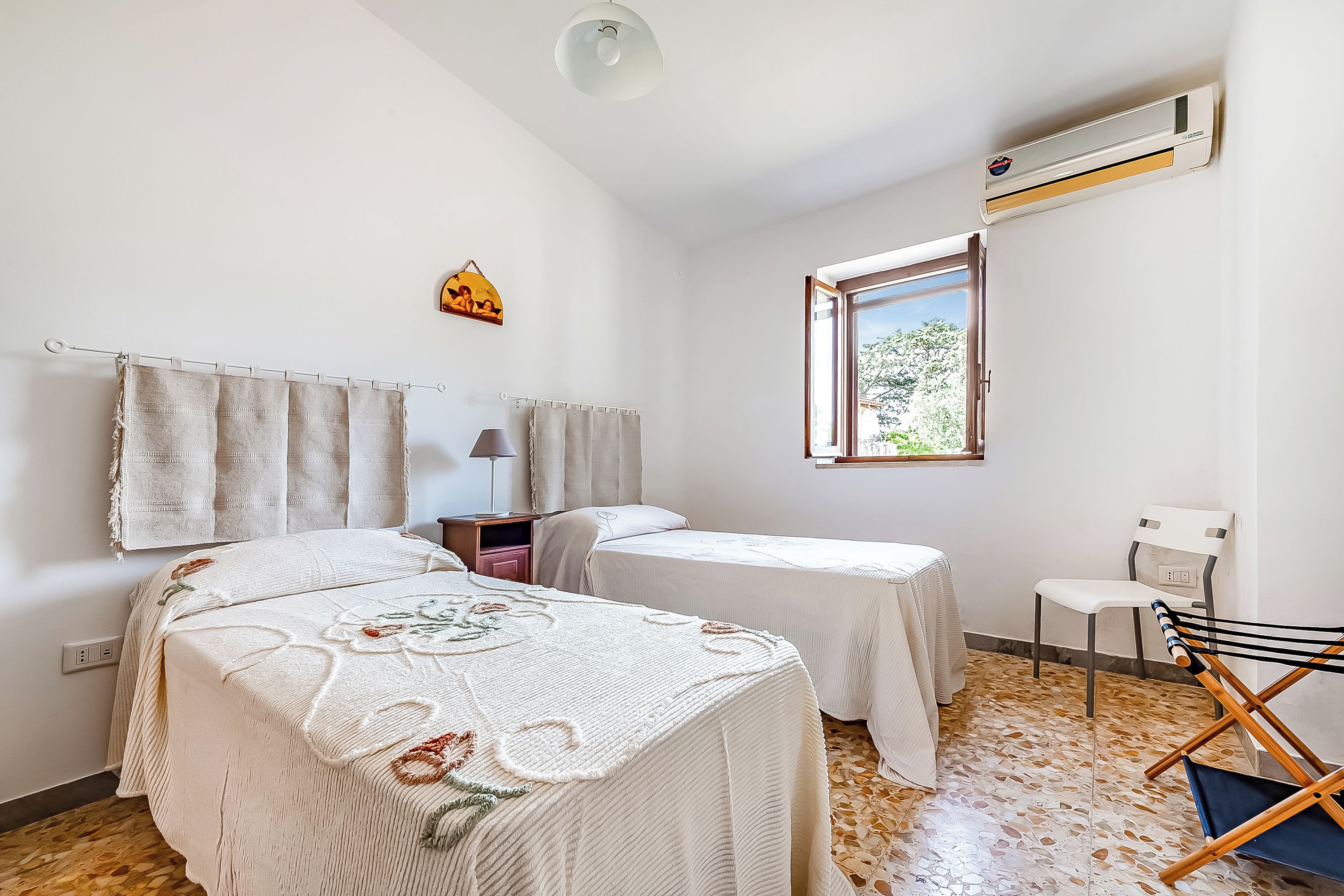 A room with two beds, a window, an air conditioner, a desk, and a chair.